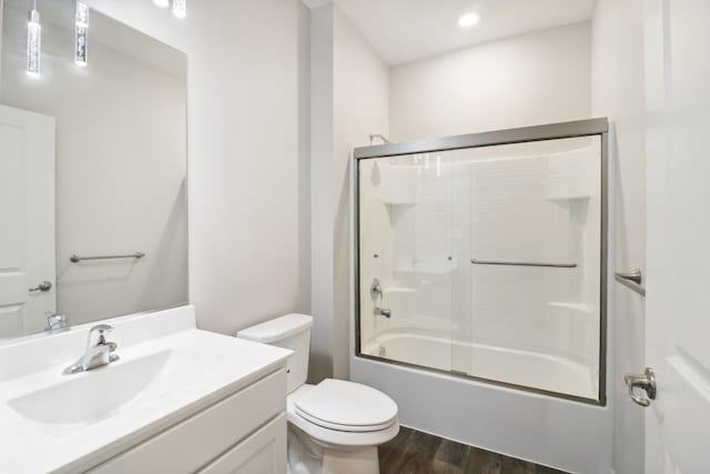 full bathroom featuring vanity, bath / shower combo with glass door, hardwood / wood-style flooring, and toilet