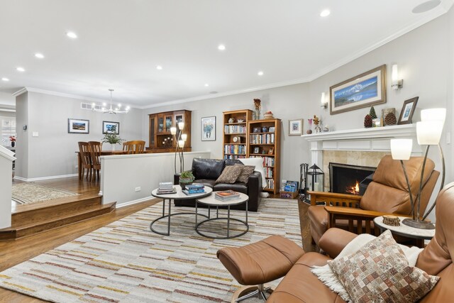 living room featuring crown molding, a notable chandelier, light wood-type flooring, and a fireplace