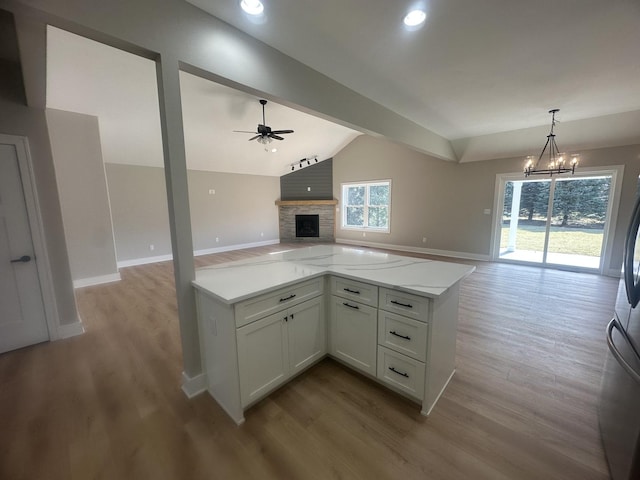 kitchen featuring white cabinetry, vaulted ceiling with beams, light stone counters, ceiling fan with notable chandelier, and decorative light fixtures