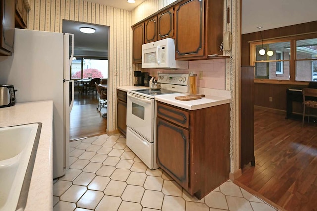 kitchen featuring light wood-type flooring, white appliances, decorative light fixtures, and sink