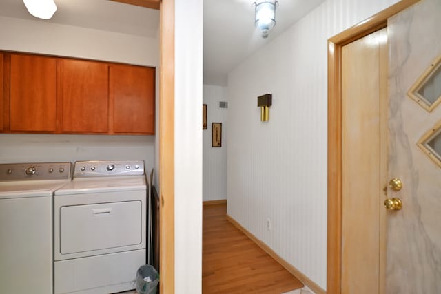 laundry area featuring separate washer and dryer, light hardwood / wood-style flooring, and cabinets