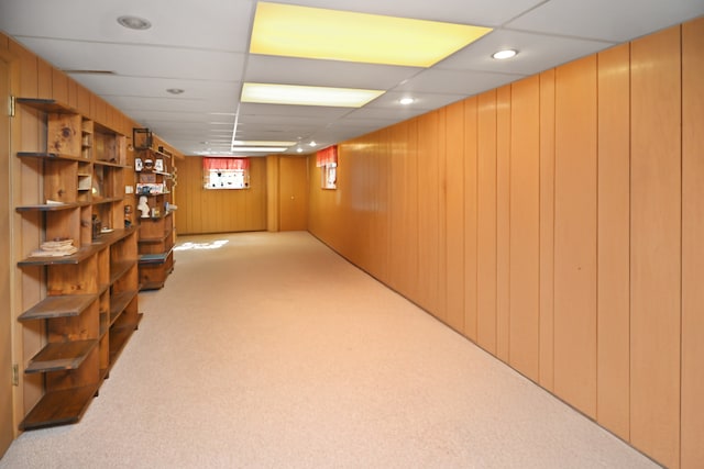 basement featuring a paneled ceiling, light carpet, and wooden walls