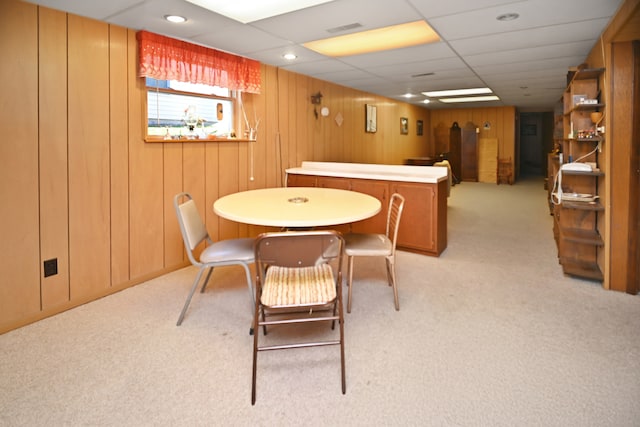 carpeted dining room with a drop ceiling and wood walls