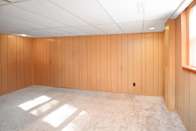 spare room with a paneled ceiling, wooden walls, and light colored carpet