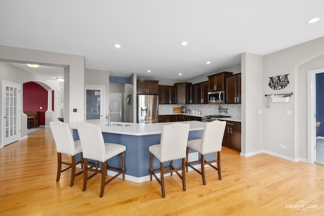 kitchen with a center island with sink, a kitchen breakfast bar, appliances with stainless steel finishes, and light wood-type flooring