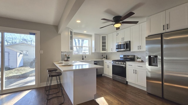 kitchen featuring white cabinets, dark wood-type flooring, stainless steel appliances, kitchen peninsula, and a breakfast bar