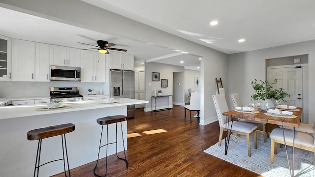 kitchen featuring appliances with stainless steel finishes, white cabinetry, dark hardwood / wood-style floors, ceiling fan, and a breakfast bar area