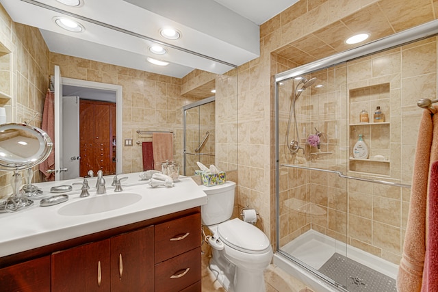 bathroom with vanity, toilet, a shower with shower door, and tile walls