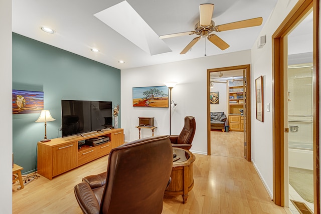 living room with ceiling fan, light wood-type flooring, and a skylight