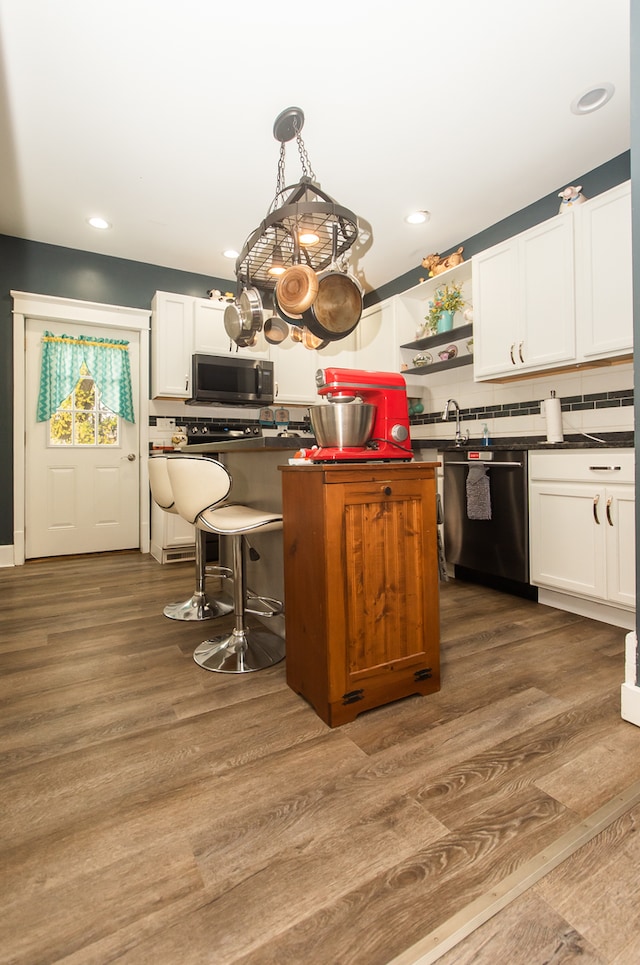 kitchen featuring hardwood / wood-style floors, tasteful backsplash, appliances with stainless steel finishes, white cabinetry, and decorative light fixtures