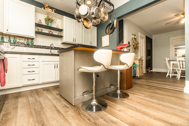 kitchen with ceiling fan, backsplash, white cabinetry, light hardwood / wood-style flooring, and sink