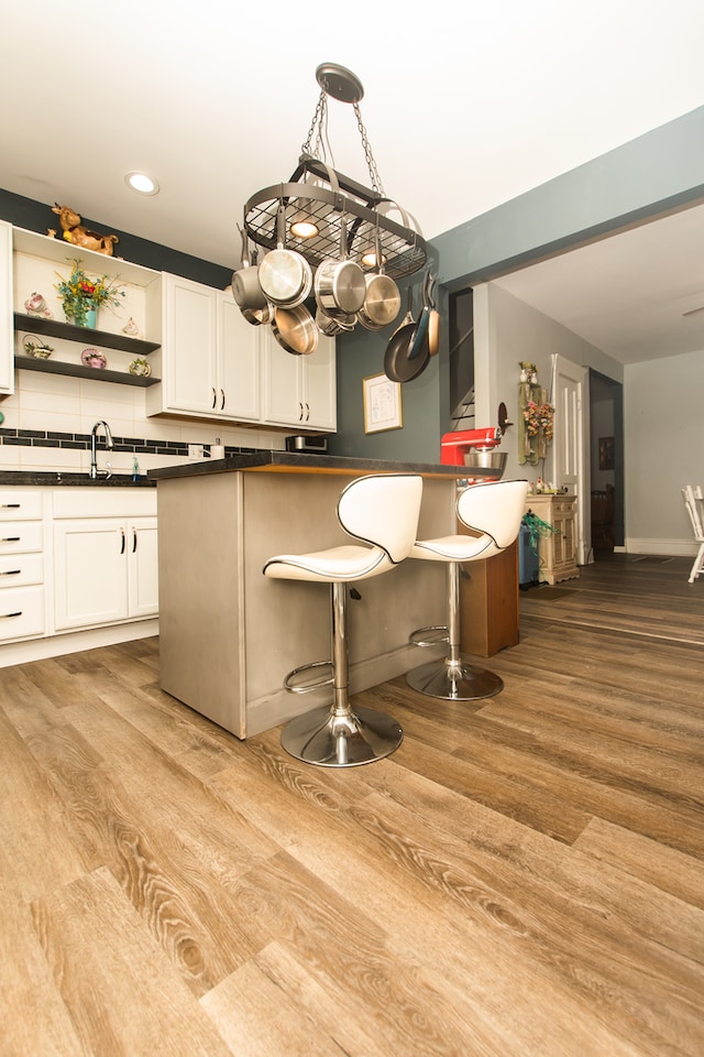 kitchen featuring tasteful backsplash, hanging light fixtures, a breakfast bar, white cabinetry, and light hardwood / wood-style floors