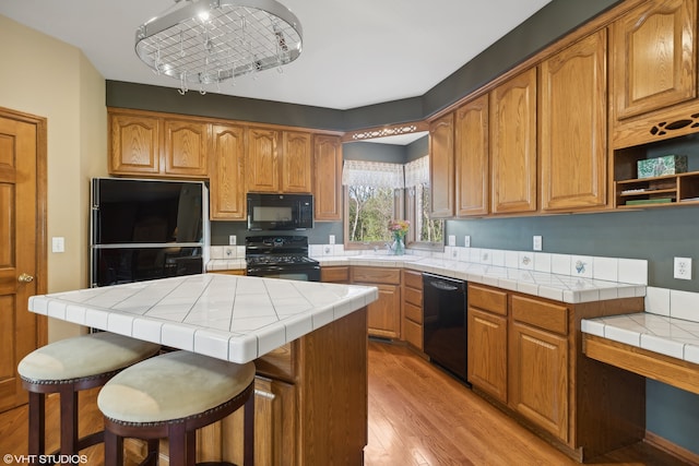 kitchen featuring black appliances, a kitchen bar, a kitchen island, tile countertops, and light hardwood / wood-style floors