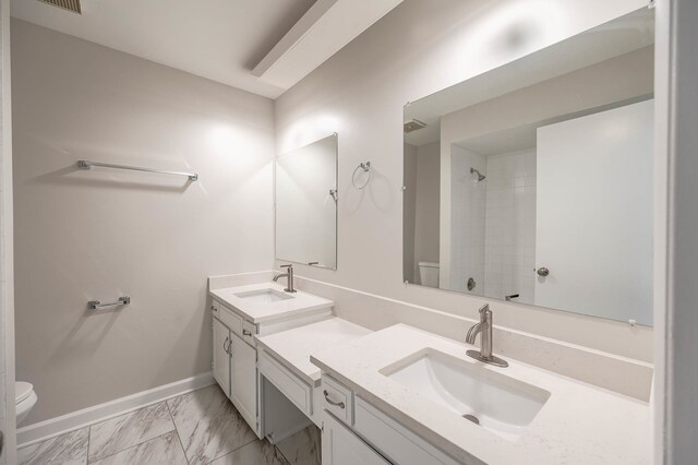 bathroom with a tile shower, vanity, and toilet