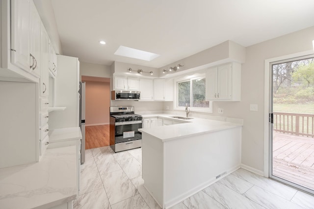 kitchen featuring a skylight, white cabinetry, appliances with stainless steel finishes, and kitchen peninsula