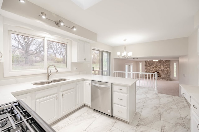 kitchen featuring a fireplace, sink, white cabinets, stainless steel dishwasher, and kitchen peninsula