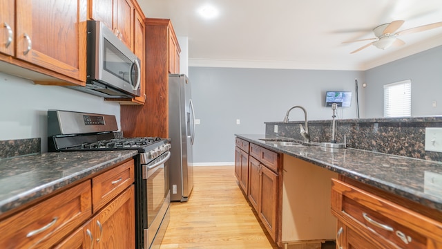 kitchen with stainless steel appliances, dark stone countertops, ornamental molding, sink, and light hardwood / wood-style floors