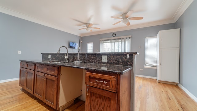 kitchen with dark stone counters, ornamental molding, sink, light wood-type flooring, and ceiling fan