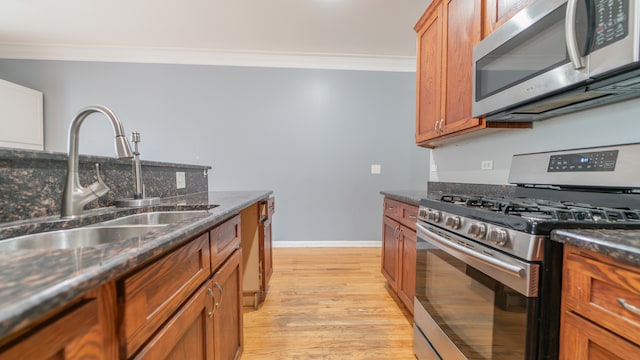 kitchen featuring appliances with stainless steel finishes, sink, light wood-type flooring, dark stone countertops, and crown molding