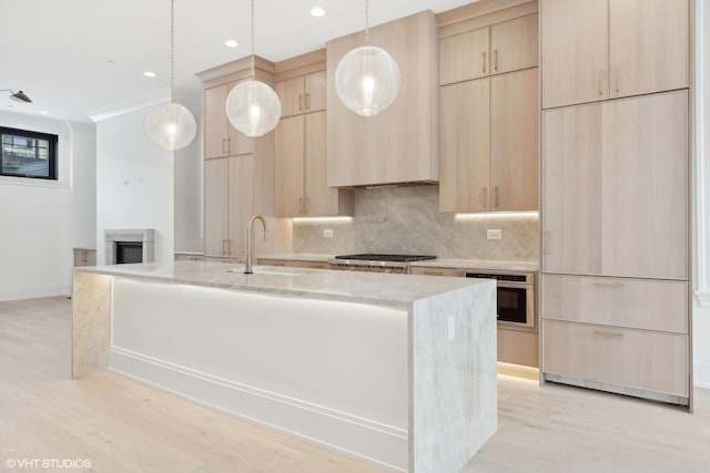 kitchen featuring an island with sink, light brown cabinetry, sink, and hanging light fixtures