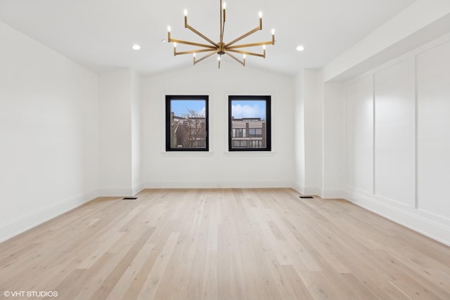 spare room featuring a chandelier, vaulted ceiling, and light wood-type flooring