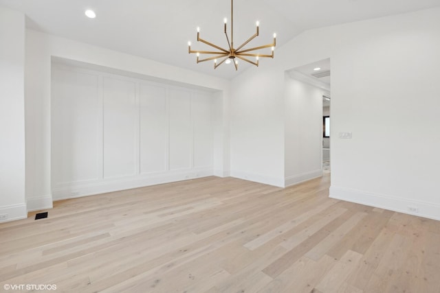 spare room featuring lofted ceiling, a chandelier, and light hardwood / wood-style floors