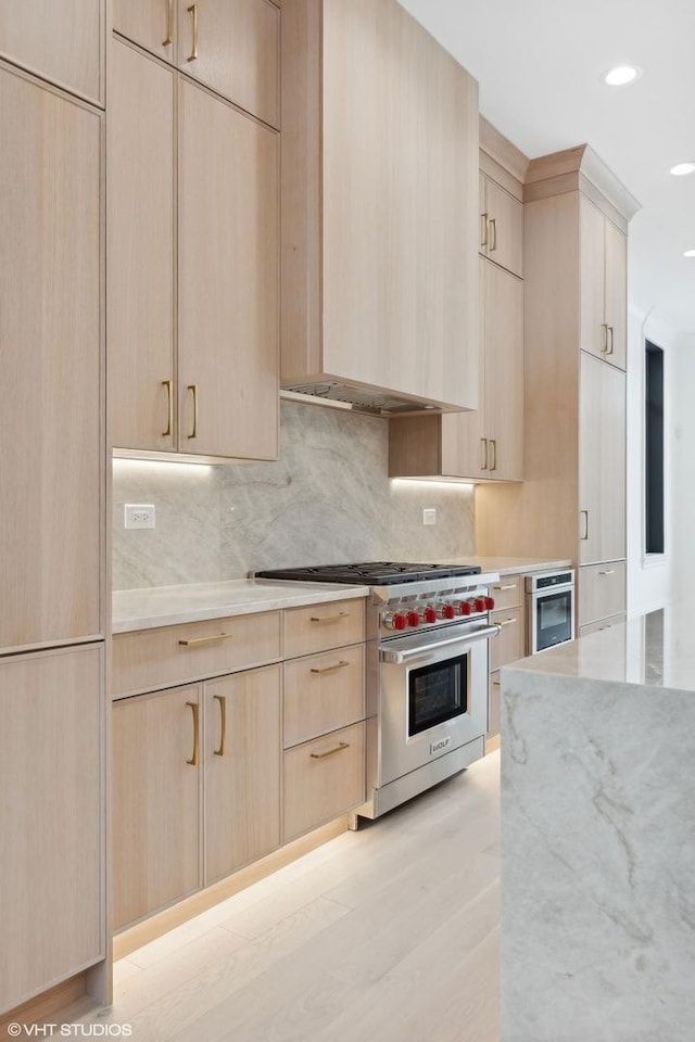 kitchen with appliances with stainless steel finishes, light brown cabinetry, light wood-type flooring, and backsplash