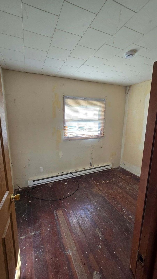 unfurnished room with dark wood-type flooring and a baseboard heating unit