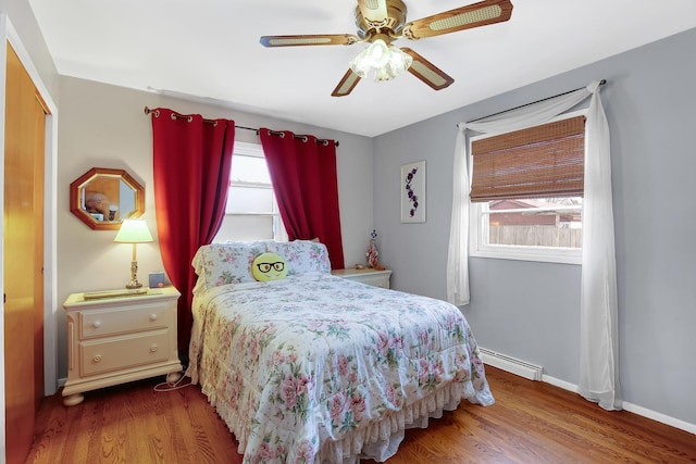 bedroom featuring multiple windows, hardwood / wood-style flooring, and a baseboard heating unit