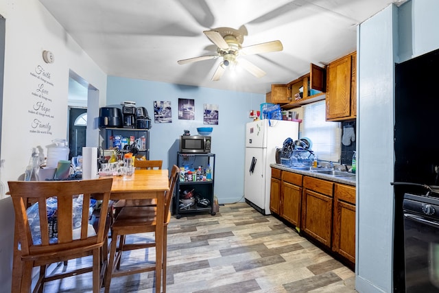 kitchen with ceiling fan, black oven, light hardwood / wood-style floors, white fridge, and sink