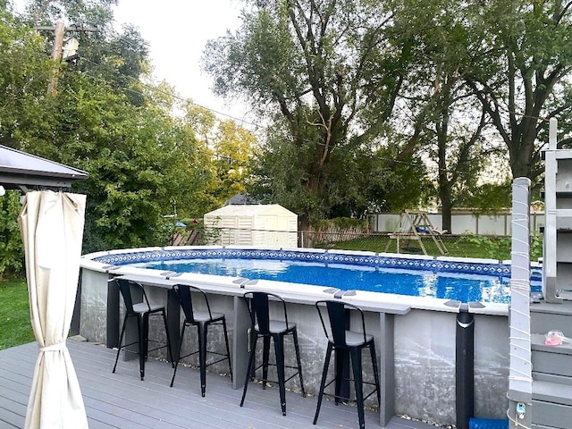 view of pool with a bar, a shed, and a deck