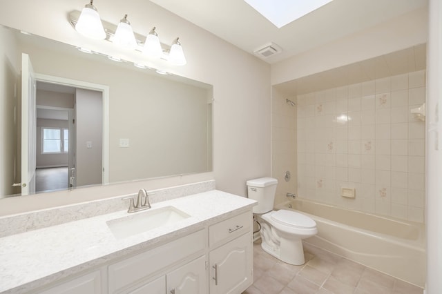 full bathroom with a skylight, toilet, vanity, tiled shower / bath combo, and tile patterned flooring