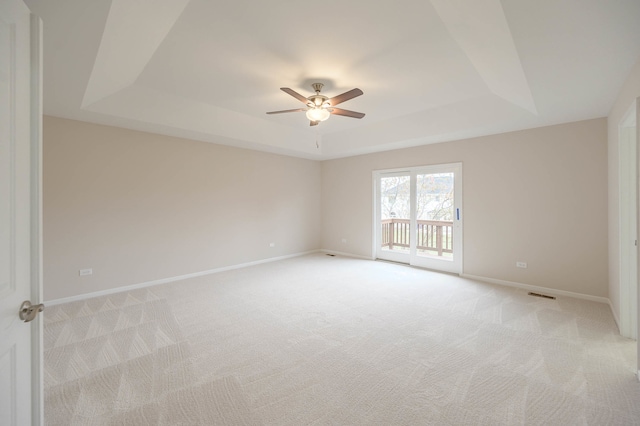 empty room with ceiling fan, light colored carpet, and a raised ceiling