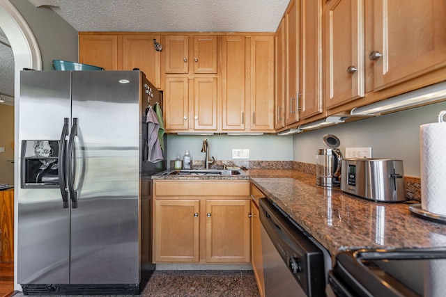 kitchen featuring appliances with stainless steel finishes, a textured ceiling, dark stone countertops, and sink