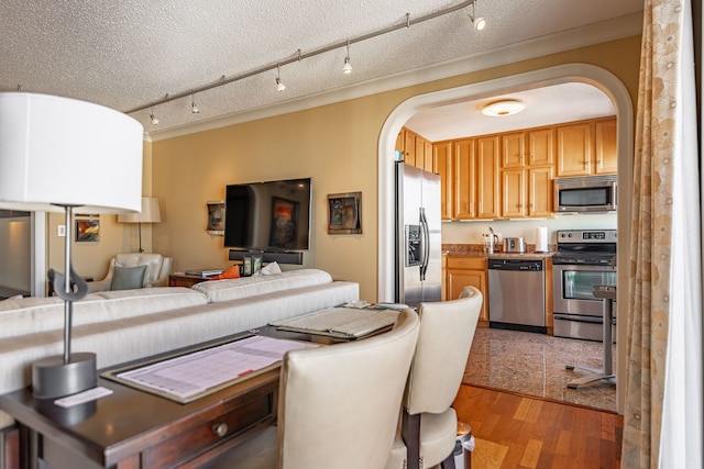 kitchen with track lighting, appliances with stainless steel finishes, a textured ceiling, wood-type flooring, and ornamental molding