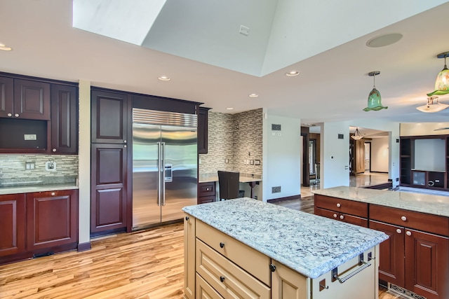 kitchen with lofted ceiling, decorative backsplash, cream cabinets, light hardwood / wood-style flooring, and built in refrigerator