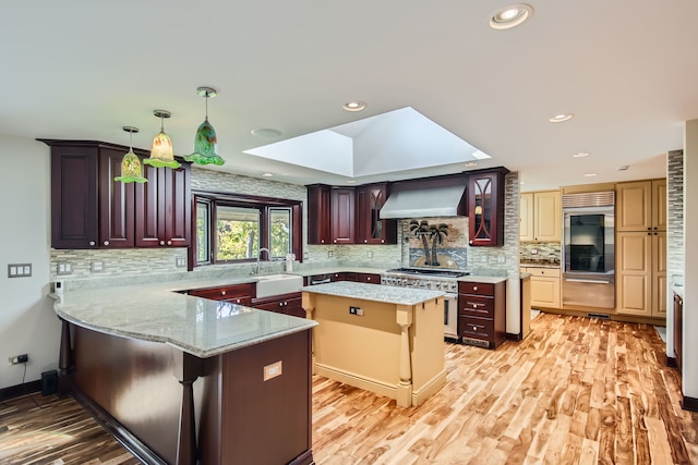 kitchen featuring a skylight, a kitchen bar, a kitchen island, high quality appliances, and wall chimney exhaust hood