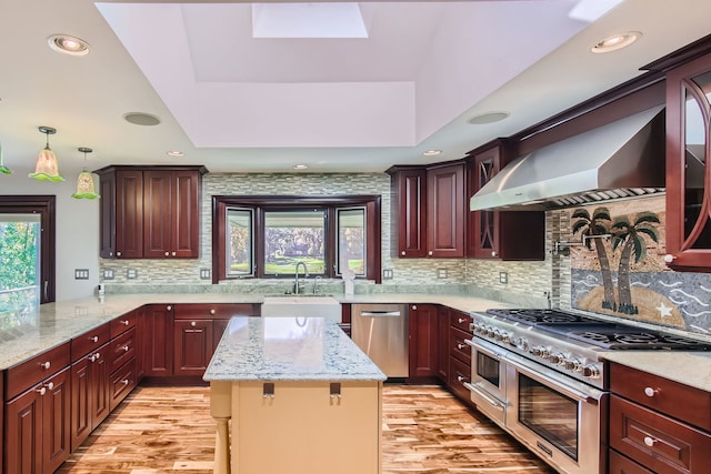 kitchen featuring wall chimney range hood, backsplash, appliances with stainless steel finishes, and a kitchen bar