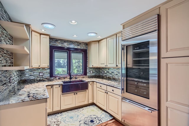 kitchen with light stone counters, decorative backsplash, sink, and cream cabinetry