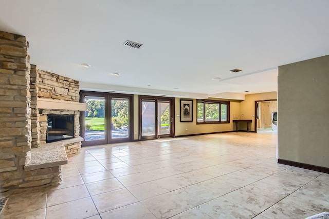 unfurnished living room featuring light tile patterned flooring, a stone fireplace, and plenty of natural light