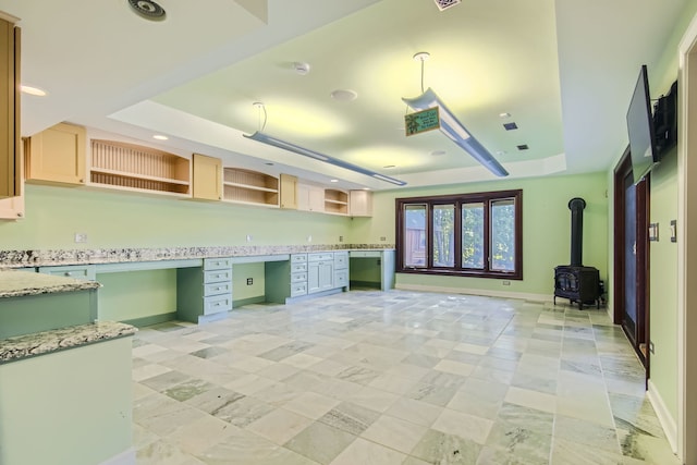 kitchen with dishwasher, built in desk, a wood stove, a raised ceiling, and light stone counters