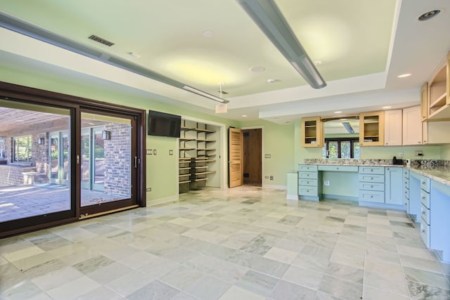 kitchen featuring built in desk, light brown cabinetry, and a tray ceiling