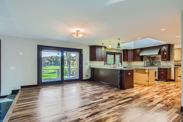 kitchen featuring wall chimney range hood, dark wood-type flooring, kitchen peninsula, backsplash, and high end range