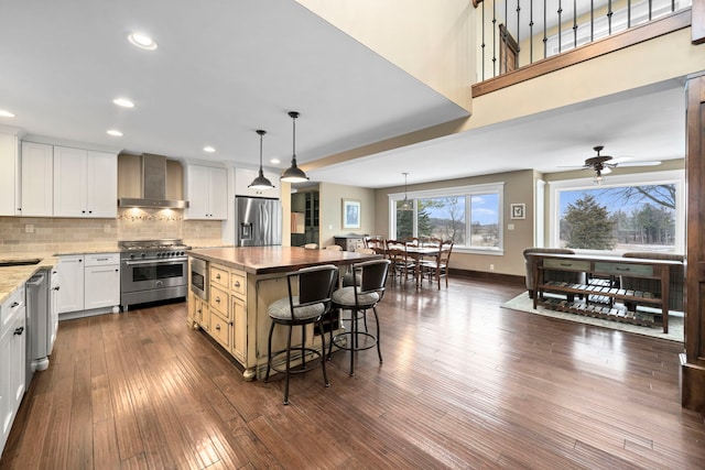 kitchen featuring pendant lighting, appliances with stainless steel finishes, wall chimney exhaust hood, white cabinets, and a kitchen island