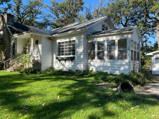 view of property exterior featuring a sunroom, a lawn, and a chimney