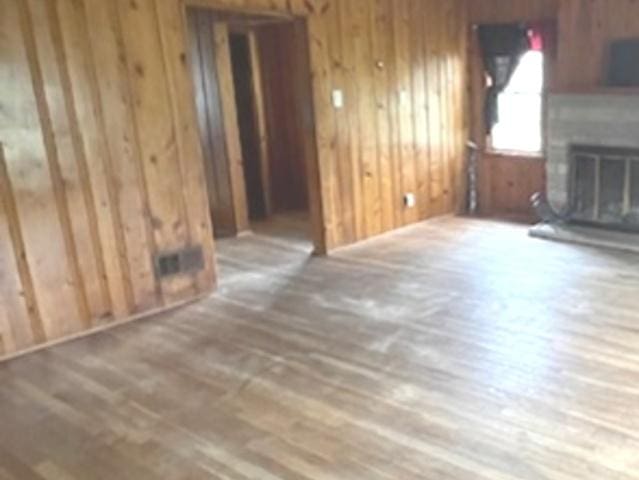 unfurnished living room with a glass covered fireplace, wood finished floors, and wood walls