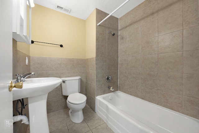 full bathroom with tile walls, tile patterned floors, a textured ceiling, toilet, and tiled shower / bath