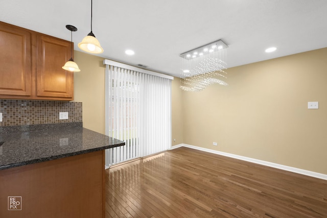 kitchen with dark stone counters, dark hardwood / wood-style floors, hanging light fixtures, a chandelier, and decorative backsplash