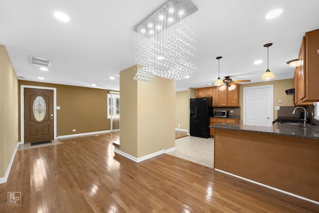 kitchen featuring black refrigerator with ice dispenser, decorative backsplash, sink, kitchen peninsula, and light hardwood / wood-style flooring