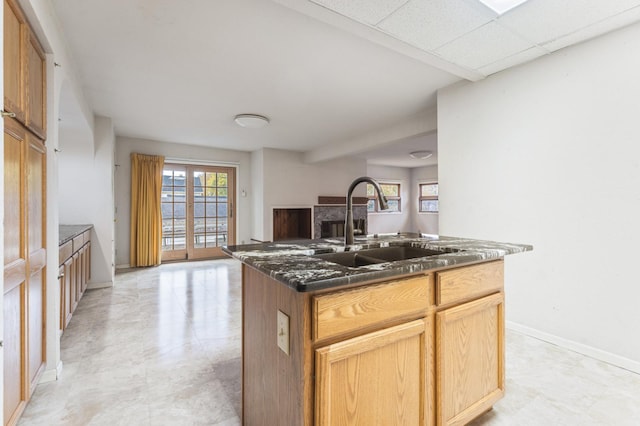 kitchen with a drop ceiling, dark stone countertops, sink, and an island with sink